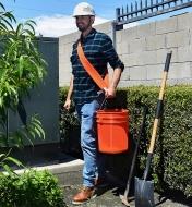 A man uses a Bucket Buddy Sash to help carry a heavy load in a pail