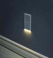 A duplex-style LED outlet cover plate mounted on a wall, giving gentle, diffused lighting at night.