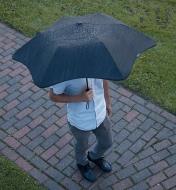 A man walks down a path in the rain carrying an XS Metro Compact Umbrella