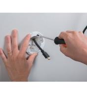 Using a screwdriver to turn the screws on the grommet after it's been placed in the wall