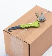 Couteau utilitaire pour porte-clés déplié accompagné de clés sur une boîte en carton fermée par du ruban adhésif
