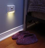 Controlled Beam PIR Light mounted on a wall beside a bed, illuminating a pair of slippers on the floor