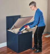 A woman places blankets inside a bench seat storage box made with the Bench Seat Hinges