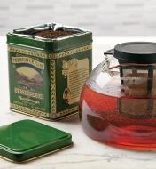 A tin of Orange Pekoe Tea beside a glass teapot with tea brewing inside