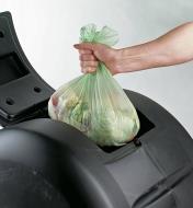 Placing a full compostable bag inside a compost bin