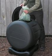 Femme jetant un sac compostable plein dans un composteur rotatif