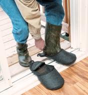 Homme enfilant un premier couvre-chaussure sur des bottes boueuses sur le seuil de la porte
