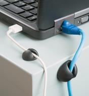 Two CableDrop Cord Clips affixed to a table, holding cords plugged into a laptop