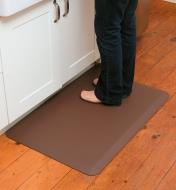 Personne debout sur un tapis antifatigue moyen brun de 24 po × 36 po devant un comptoir