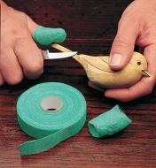 A person with high-friction guard tape on their thumb carving a wooden bird