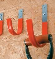 Several Heavy-Duty Strap Hooks mounted to a garage wall, one of them holding a D-handle tool