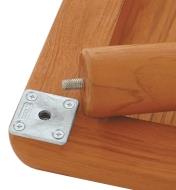 Plaque de fixation carrée pour patte de meuble fixée sous un plateau de table près d’une patte prête à être vissée