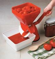 Personne tournant la manivelle d'un presse-tomates pour broyer des tomates entières et en récupérer la pulpe dans un bol