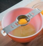 Egg separator sits on a bowl, with a yolk in the slotted cup and egg white underneath in the bowl