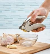 Using the garlic press to mince garlic into a bowl