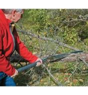 Homme sciant un arbre tombé avec une scie pliante pour sentier