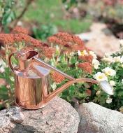 Haws Copper Watering Can sitting on a rock in a flower garden