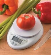 Tomate posée sur une minibalance de cuisine numérique près d'autres légumes et d'un couteau