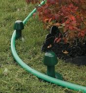 A hose looped around two hose guides beside a garden bed
