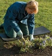 A woman kneels on on the Kneeling Strip while gardening