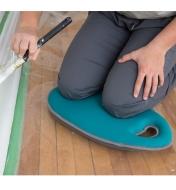 A person kneels on the Teal Kneeling Pad while painting trim in a house