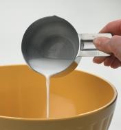 Personne versant du lait dans un bol à mélanger avec une tasse à mesurer