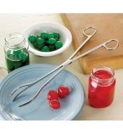 Kitchen Tongs resting on a plate beside two jars of maraschino cherries