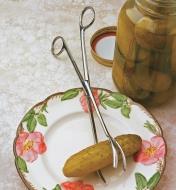 Kitchen Tongs resting on a plate, with a pickle they were used to remove from a jar