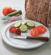 Lunchbox Pocket Knife sitting on a plate with sliced berries and vegetables next to a lunch bag