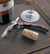 Pulltap Double-Lever Corkscrew lying next to a cork, a wine bottle and a glass