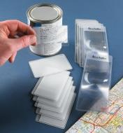 Six credit card magnifiers and six bookmark magnifiers spread on a table, beside a road map and a can with small writing on the back