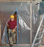 A worker walks through an open plastic doorway that seals with a Peel-and-Stick Zipper