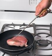 Turning a pork chop in a frying pan using a Pigtail Flipper