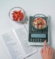 Nutritional Scale weighing a bowl of granola and strawberries, with the guide lying open next to it