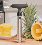 Ratcheting Pineapple Corer & Slicer on a counter beside cored and sliced pineapple