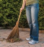 A woman sweeps debris from a patio using an Outdoor Broom