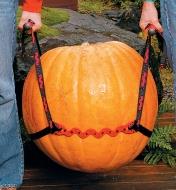 Two people using the PotLifter to carry a large pumpkin