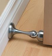 Satin chrome doorstop installed on a baseboard, holding a door open