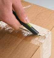 Desk Utility Cutter being used to slice through packing tape on a cardboard box