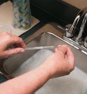 Using a straw brush and soapy water to clean out a drinking straw 