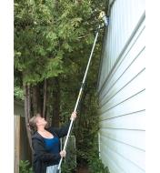 A woman holds a pole with a spray can attached to reach the upper level of a house