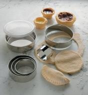 Jeux d'emporte-pièce en acier inoxydable près d'une abaisse de pâte, d'un cercle de pâte et de tartelettes cuites
