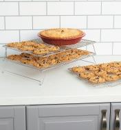 Two stacked racks holding cookies and a pie next to a third rack sitting on the counter, holding cookies