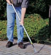 A man using the Telescoping Crack Weeder to remove weeds from between patio stones