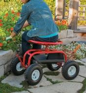 A woman sitting on a Steerable Rolling Seat tends a raised flower garden