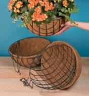 Two empty 18" hanging baskets on a table and one holding a plant being hung up