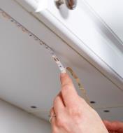 Mounting LED tape lighting to the underside of a cupboard using its peel-and-stick backing