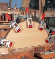 Five Bessey edge clamps being used to hold edging in place on a curved workpiece