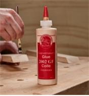 Applying 2002 GF glue to a piece of wood in the background of a glue bottle on a workbench