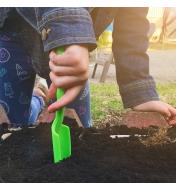 A child uses the narrow trowel from the Little Market Gardener Kit to dig in garden soil